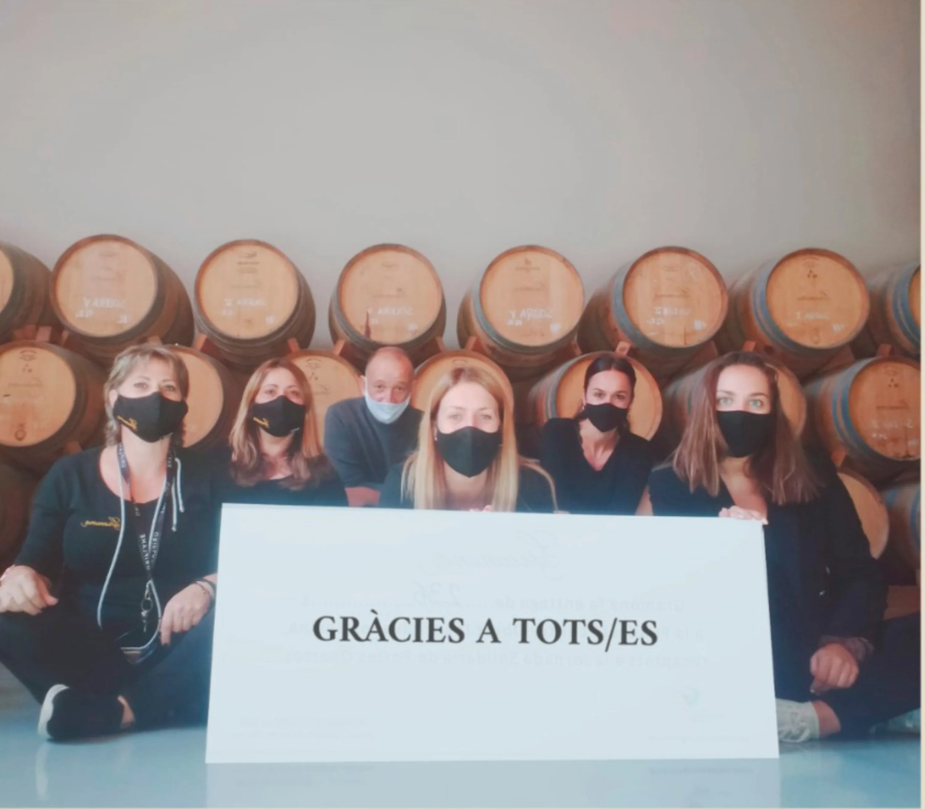 Equipo de una bodega con un cartel de agradecimiento entre barricas
